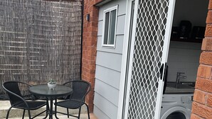 A patio with a table and chairs, a washing machine, and a door with a security screen. - Cosy Private Studio (West Bathurst)