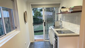 A compact living space with a kitchenette, a sofa, a trash bin, and a sliding glass door leading to an outdoor area. - Cosy Private Studio (West Bathurst)