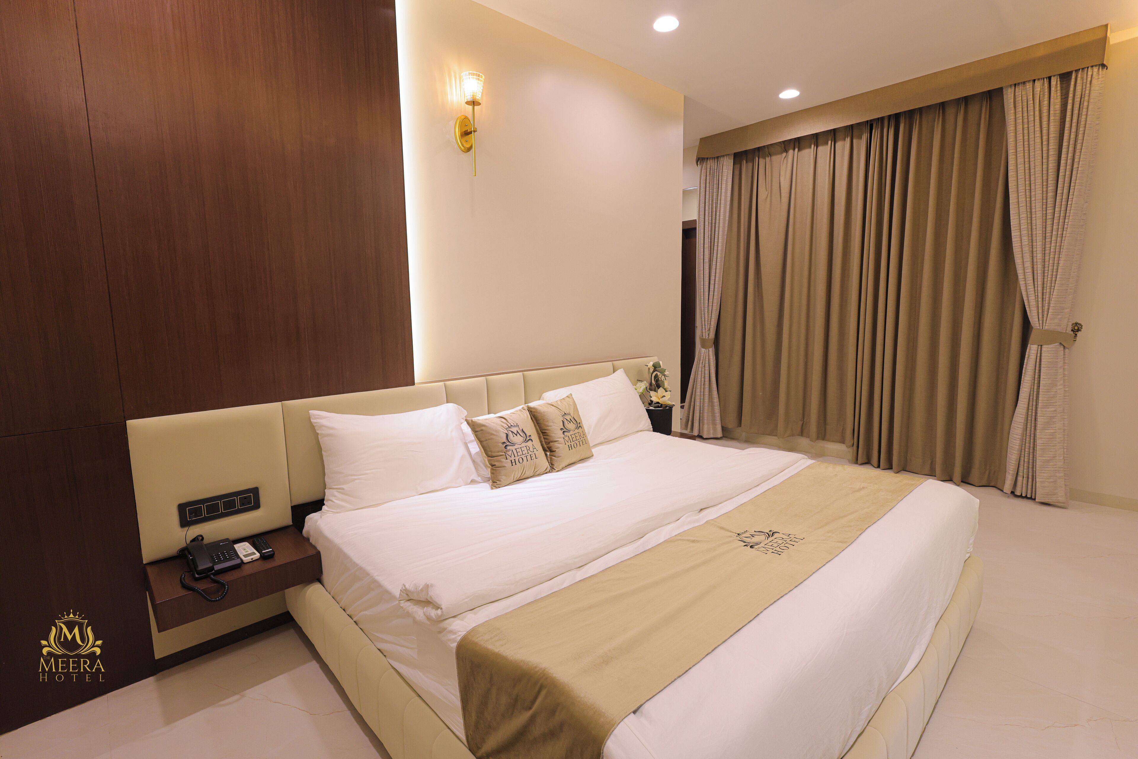 A hotel room with a large bed, a bedside table with a phone, and a wall-mounted light fixture.