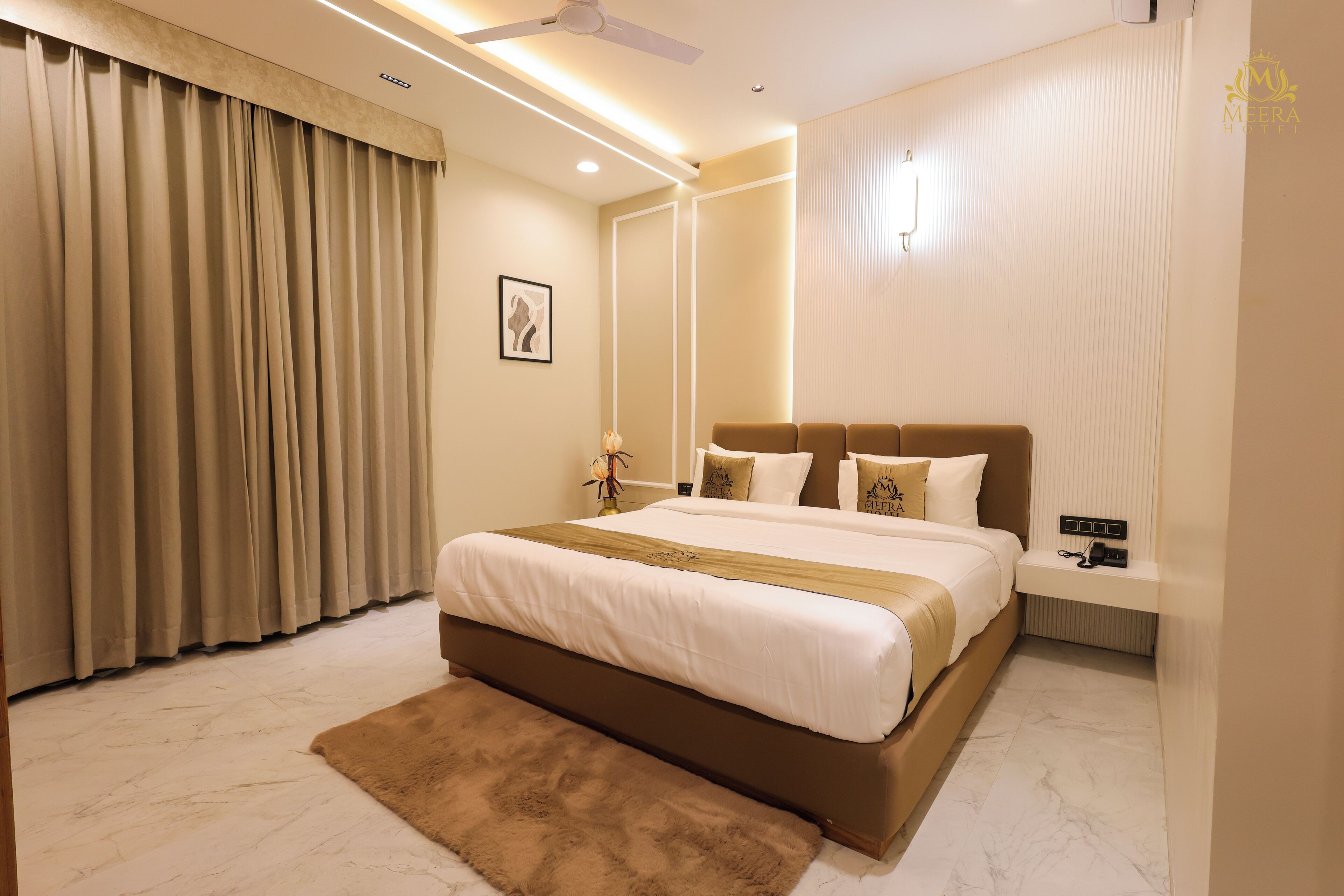 A modern hotel room with a large bed, a bedside table, a nightstand, a wall-mounted light, and a ceiling fan.