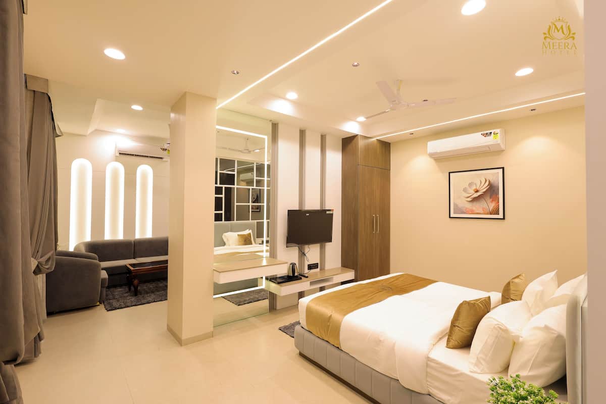 A modern hotel room with a bed, a TV, a desk, and a seating area.
