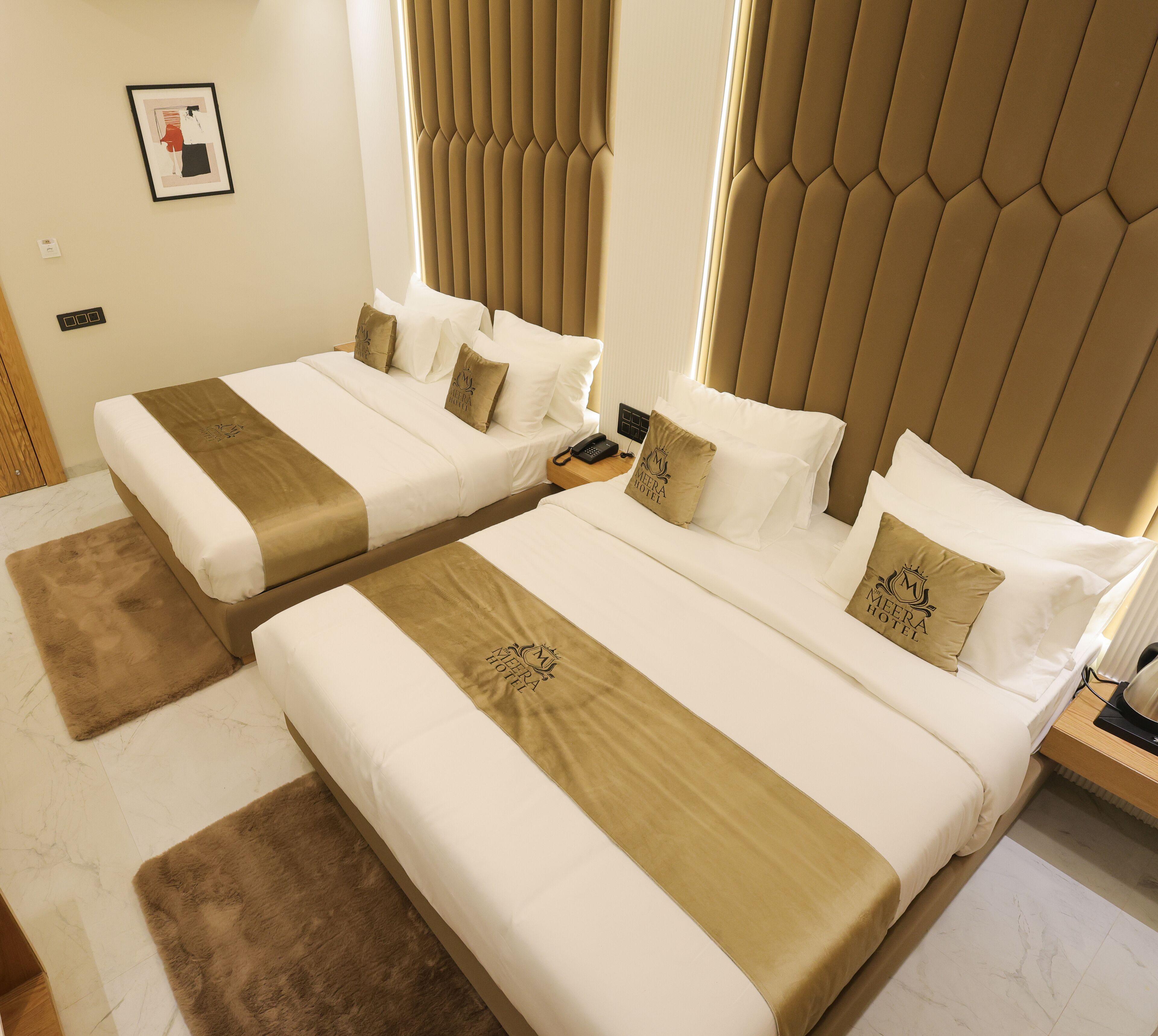 A hotel room with two beds, each with a beige and white bedspread, a brown throw blanket, and a pillow with the hotel logo.
