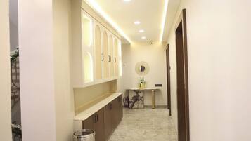 Un pasillo con piso de mármol, un mueble de pared con paneles iluminados, una pequeña mesa con un florero y un cesto de basura.