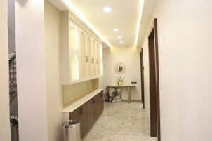 Un pasillo con piso de mármol, un mueble de pared con paneles iluminados, una pequeña mesa con un florero y un cesto de basura.