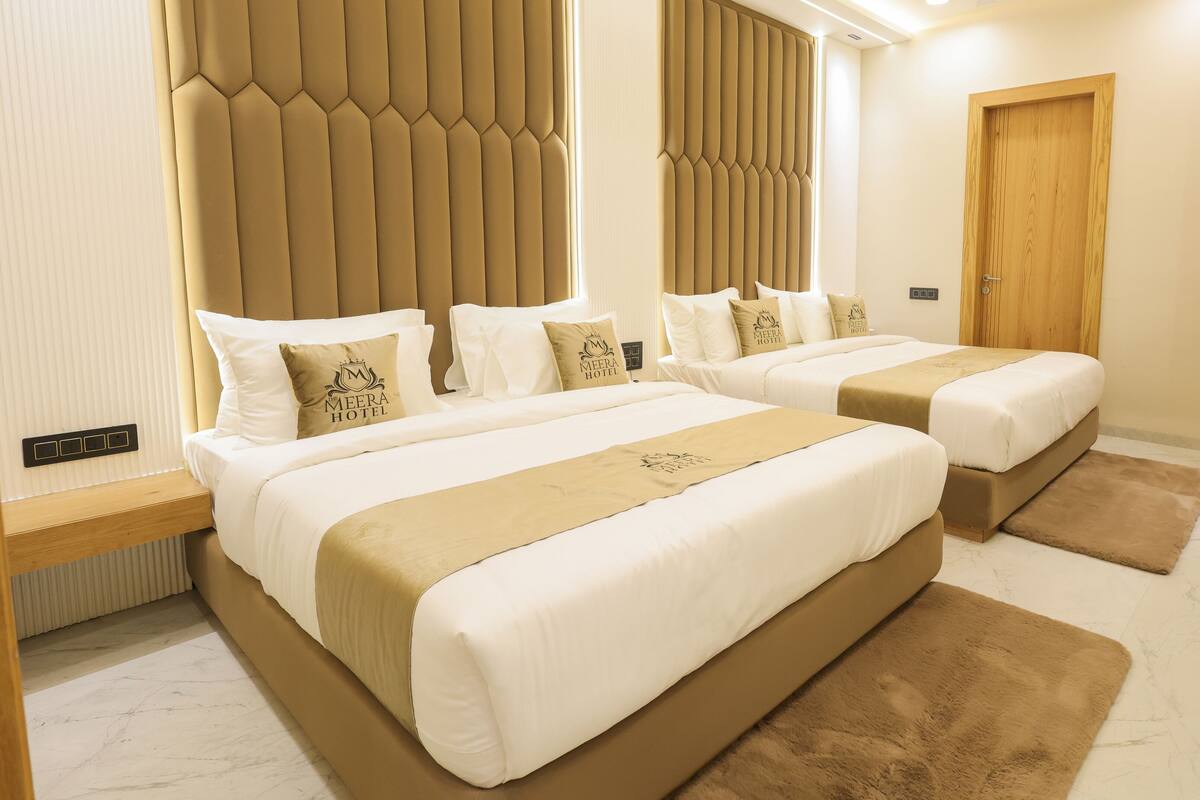 A hotel room with two beds, beige bedding, a wooden door, and a small desk with a chair.