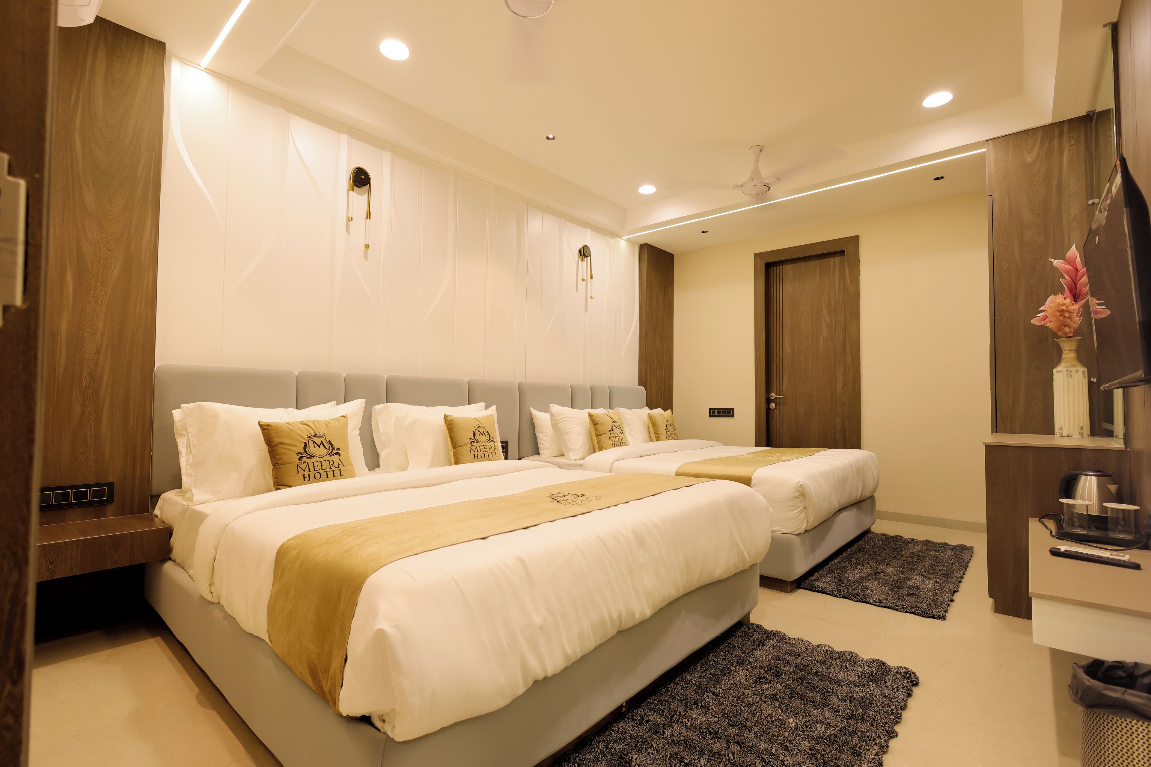 A hotel room with two beds, a wooden nightstand, a desk with a chair, a TV, and a decorative vase.