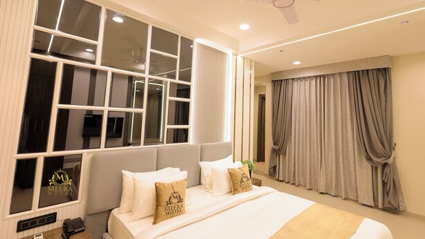A hotel room with a large bed, a ceiling fan, and a window with multiple panes. - The Meera Hotel (Ujjain)