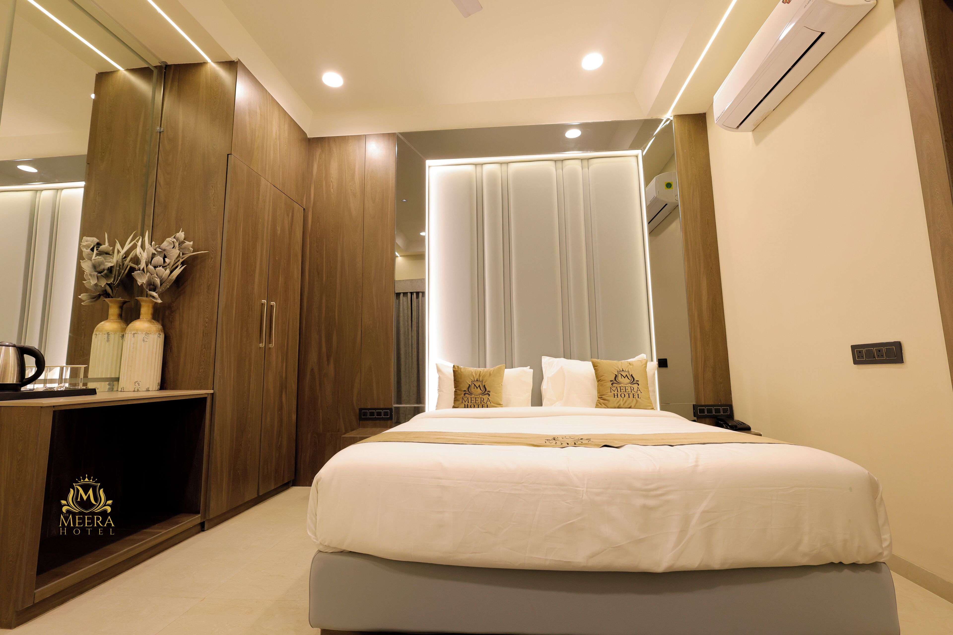 A modern hotel room with a large bed, wooden wardrobe, and a vanity area with a mirror.