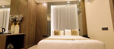 A modern hotel room with a large bed, wooden wardrobe, and a vanity area with a mirror.