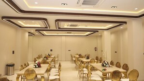 A large, well-lit conference room with long tables and golden chairs, equipped with air conditioning and a fire extinguisher. - The Meera Hotel (Ujjain)