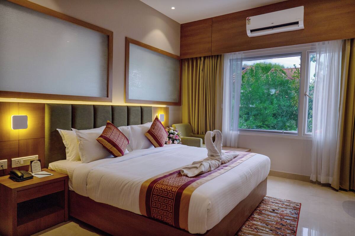 Habitación de hotel con una cama grande, una mesita de noche con lámpara, una ventana con cortinas y un equipo de aire acondicionado.