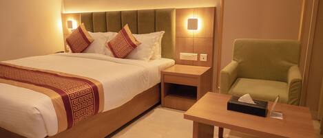 A hotel room with a large bed, a green armchair, a wooden nightstand, and a bedside table with a tissue box.