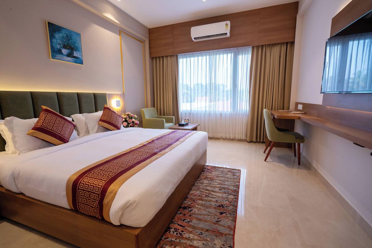 Habitación de hotel con una cama grande, un escritorio, una silla, un televisor y una ventana con cortinas.