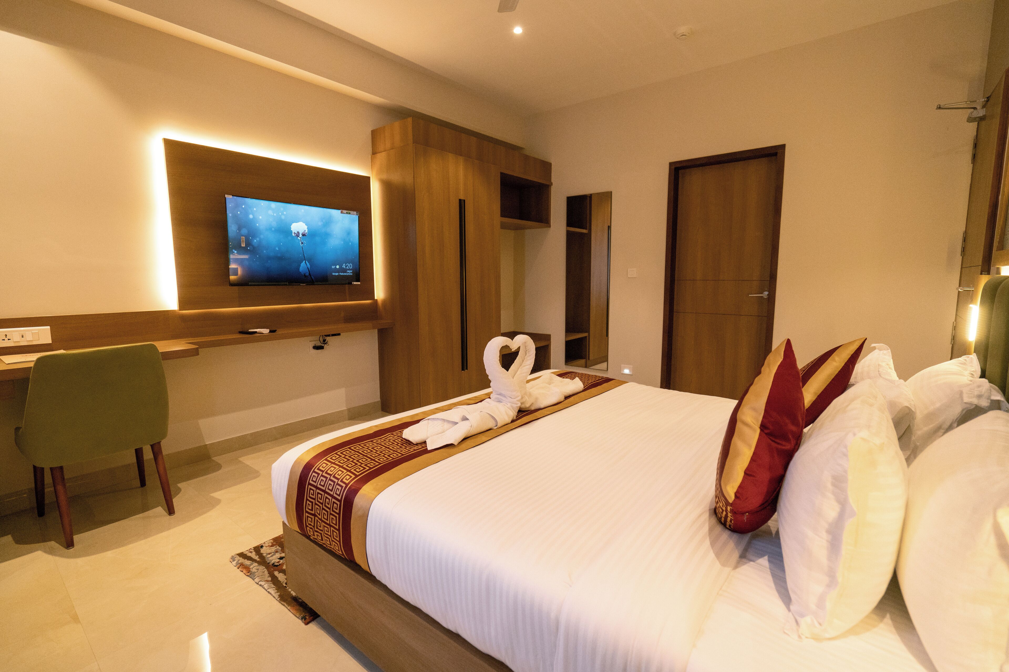 Een hotelkamer met een groot bed, een flatscreen televisie aan de muur, een bureau met stoel, en een houten garderobe.