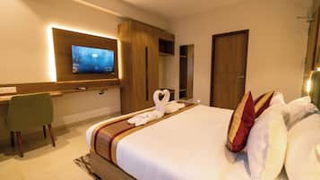 Een hotelkamer met een groot bed, een flatscreen televisie aan de muur, een bureau met stoel, en een houten garderobe.