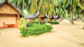 A resort with thatched-roof huts, a sandy pathway, and lush greenery.