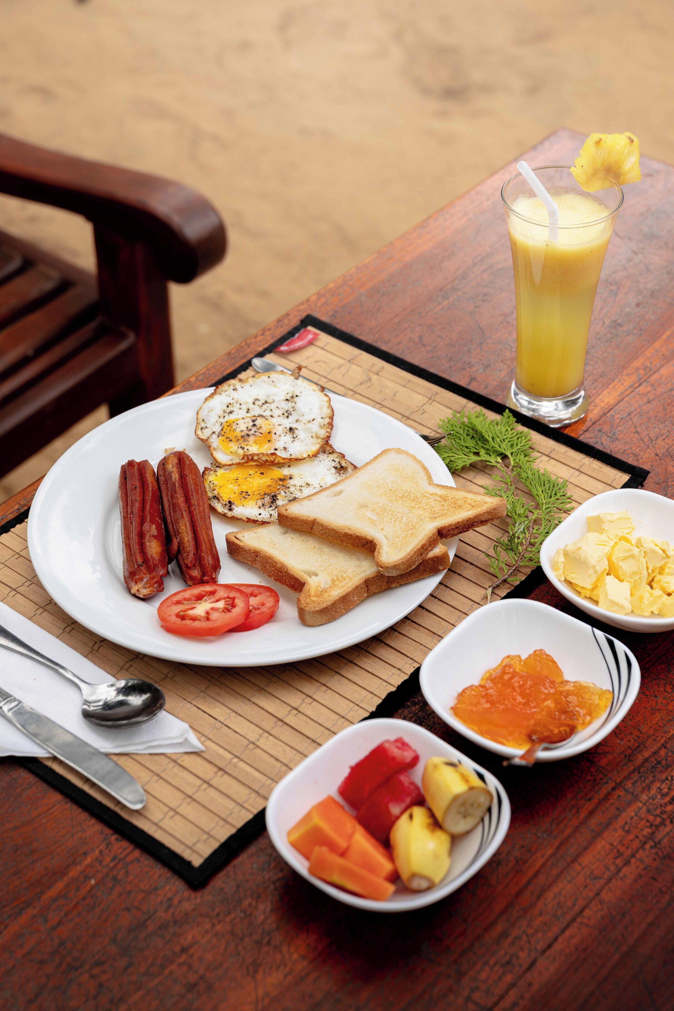 Un plato de desayuno con huevos, tocino, tostadas y tomates, junto con un vaso de zumo de naranja y diferentes acompañamientos.