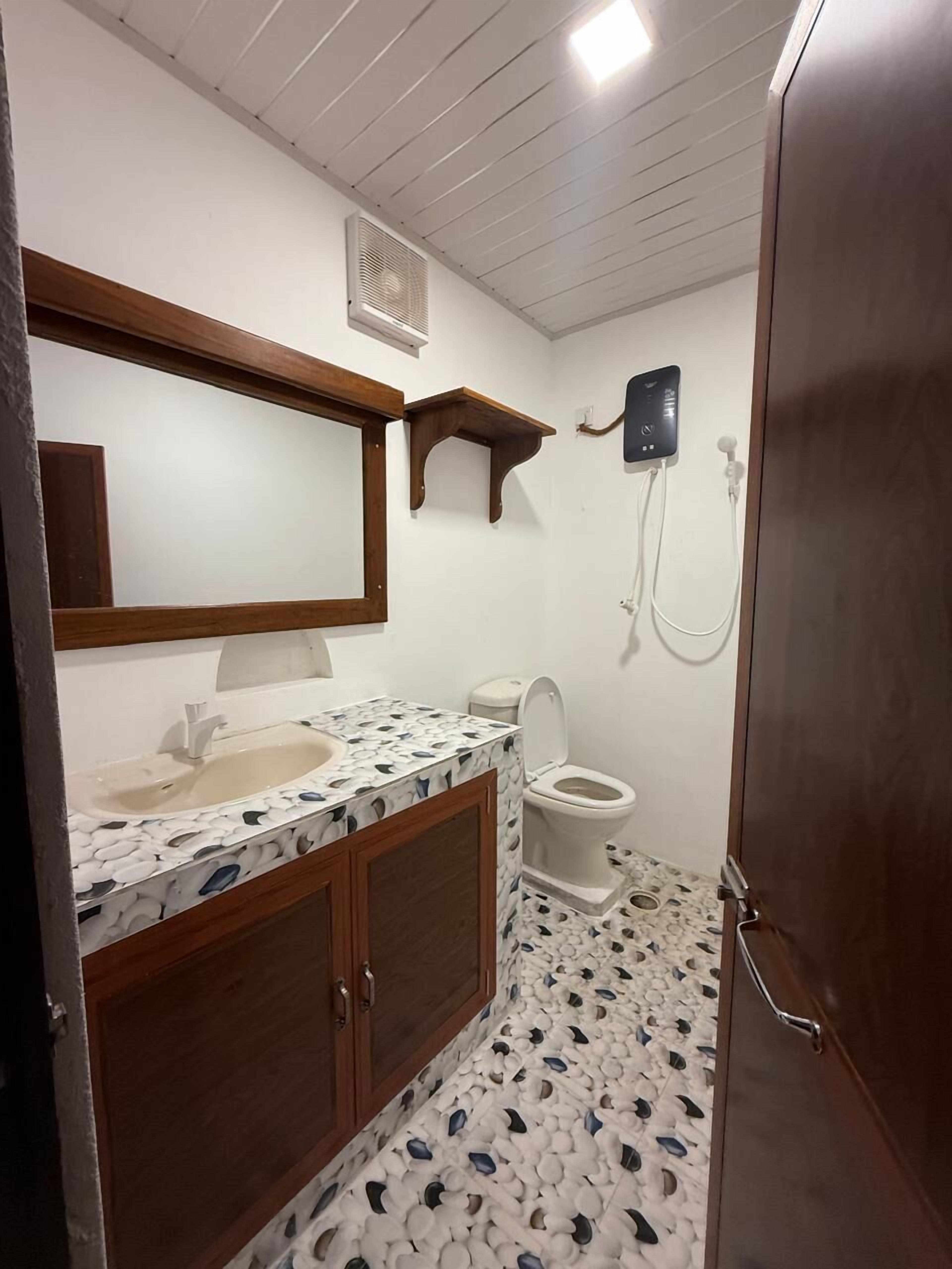 A bathroom with a white sink, wooden cabinets, a mirror, a toilet, and a shower area.