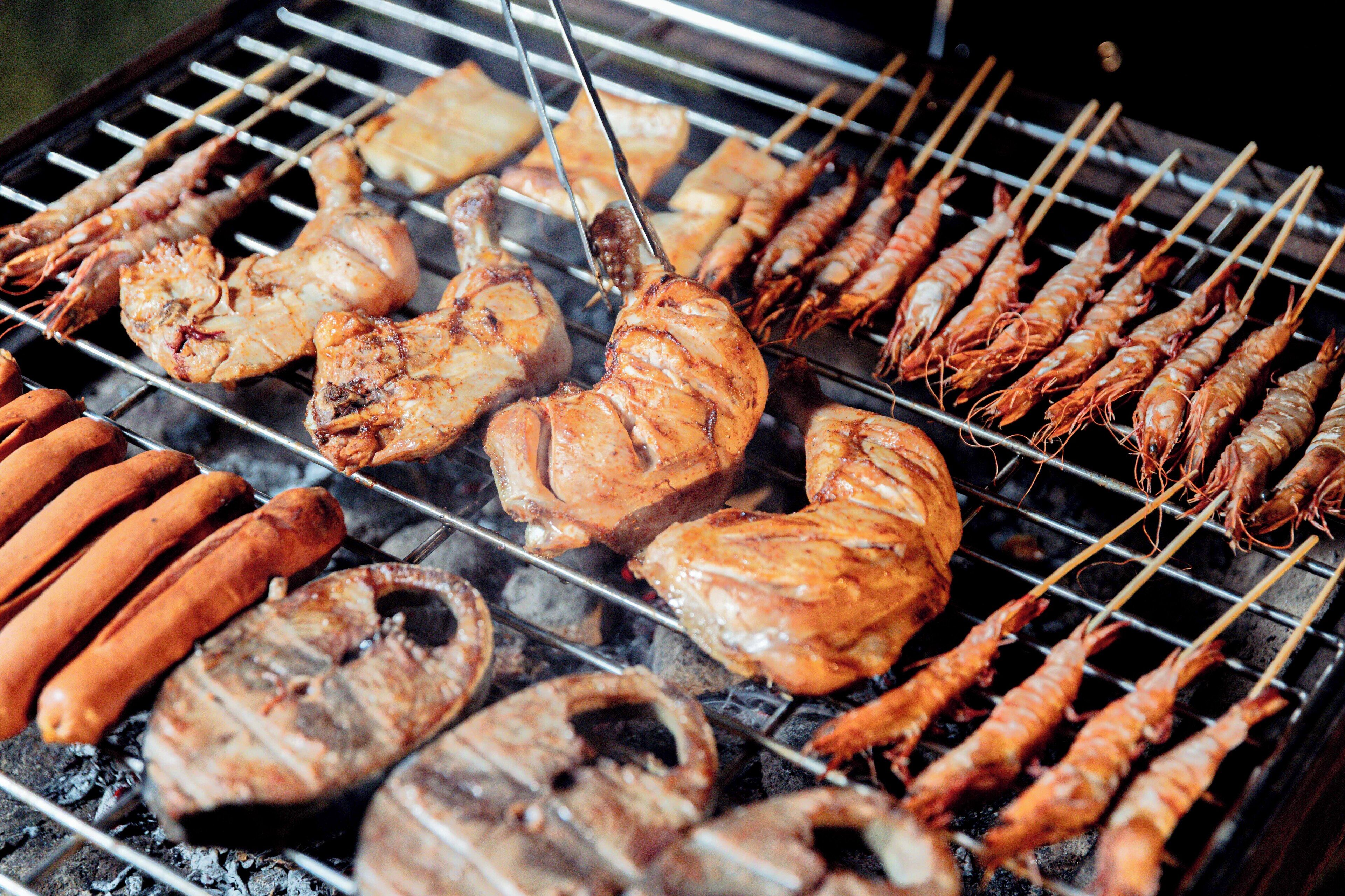 A grill with various meats and seafood being cooked.