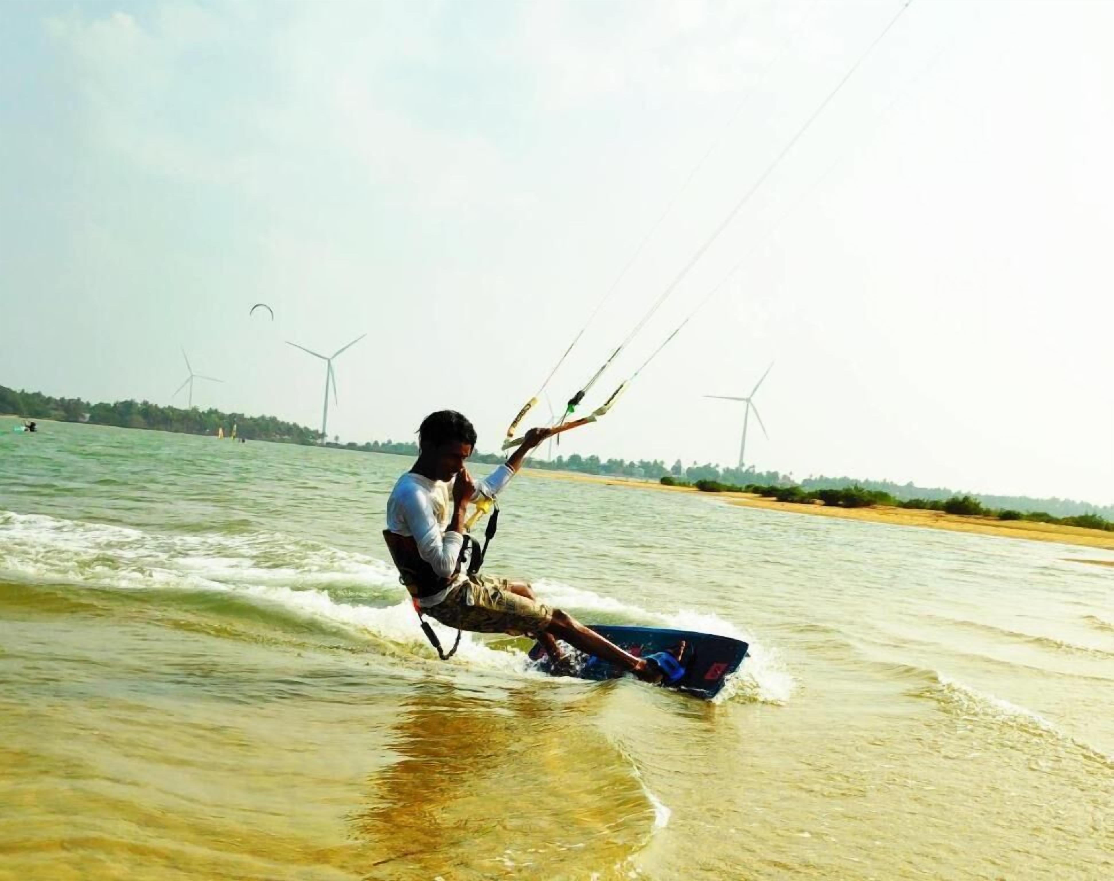 A person windsurfing on a body of water with wind turbines in the background.