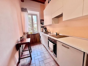 A compact kitchen with a window, a sink, a stove, and a small dining table.
