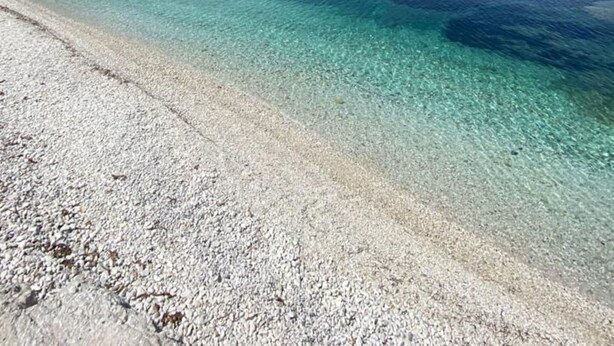Una spiaggia con acque cristalline turchesi, sabbia bianca e un promontorio roccioso.