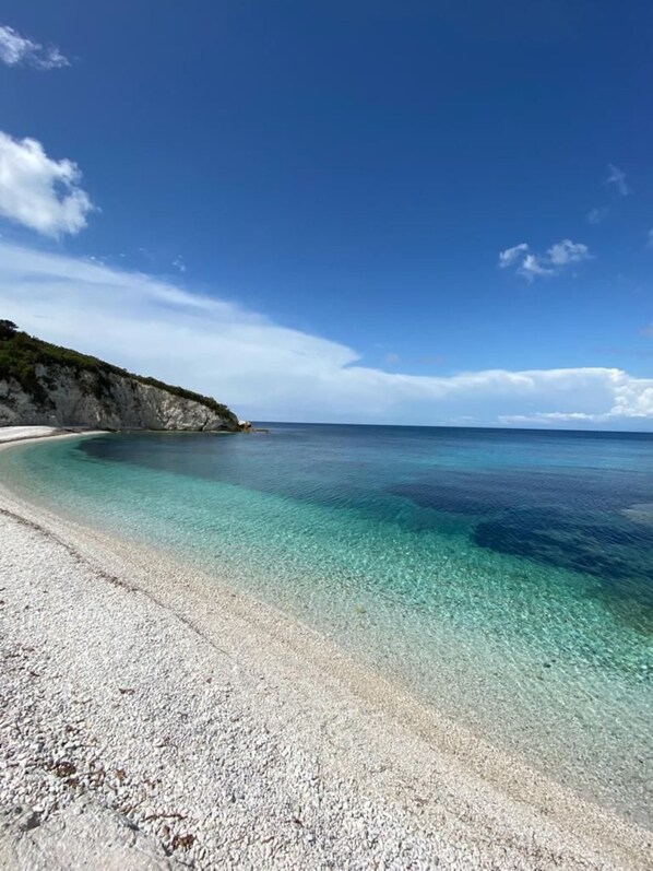 A beach with clear turquoise water, white sand, and a rocky cliff.
