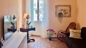 Un soggiorno con TV, lampada, divano e finestra con tende.