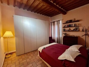 Ein Schlafzimmer mit Bett, Kleiderschrank, Lampe, Stuhl und Regal mit Büchern und Dekoration.
