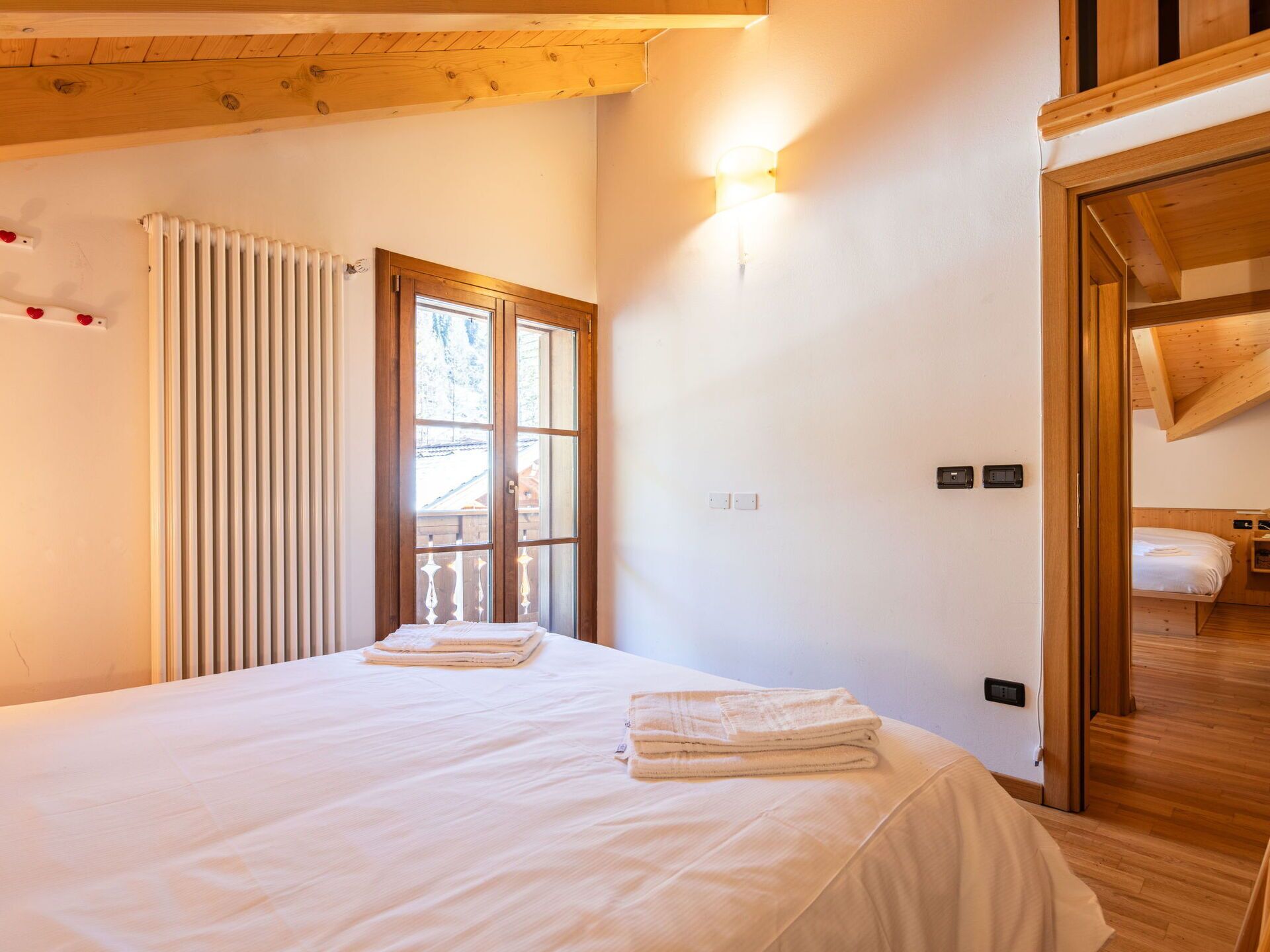 Un dormitorio con cama, ventana con persianas, luz empotrada en la pared y techo de madera.