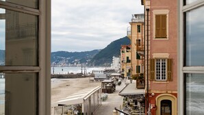 Une rue côtière bordée d’immeubles, avec une plage et une montagne en arrière-plan.