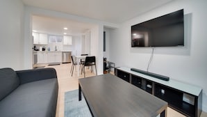 Un salon moderne avec un téléviseur à écran plat fixé au mur, une table basse en bois foncé et un canapé gris.