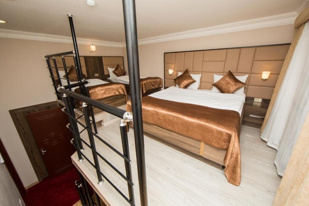 A hotel room with a large bed, a headboard with a light fixture, a wooden wardrobe, and a red carpet.