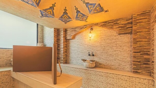 Una habitación con un escritorio de madera, una computadora portátil, un techo decorativo y una pared de ladrillo con una lámpara.