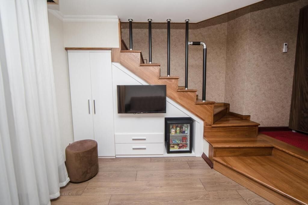 Eine Treppe mit Holzbodenstufen und schwarzen Geländern, ein weißes Schranksystem mit Fernseher und einem kleinen Kühlschrank.