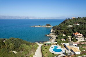 A coastal property with a swimming pool, a beach, and a view of the sea and mountains.