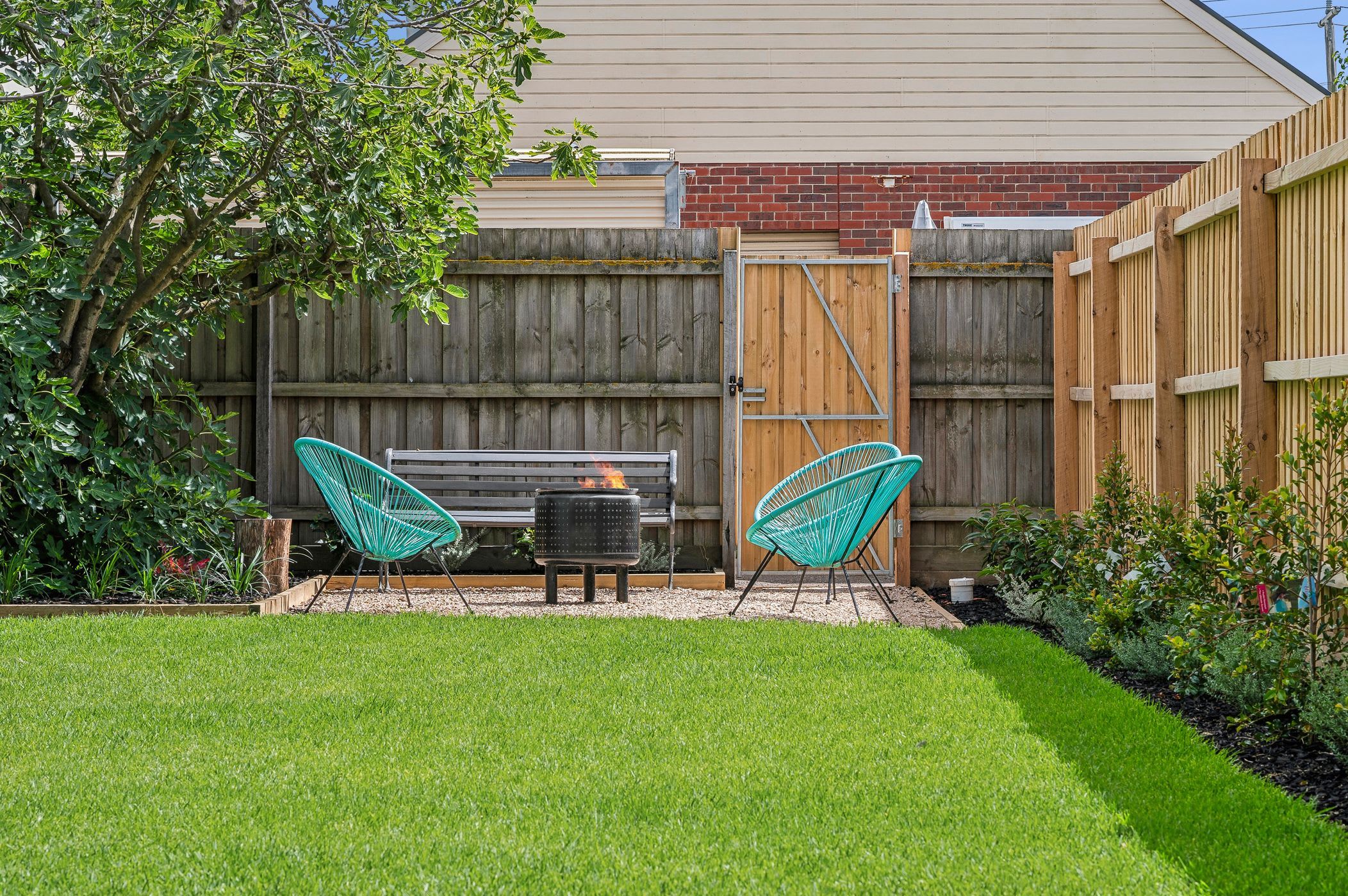 A backyard with a wooden fence, a bench, and two chairs.