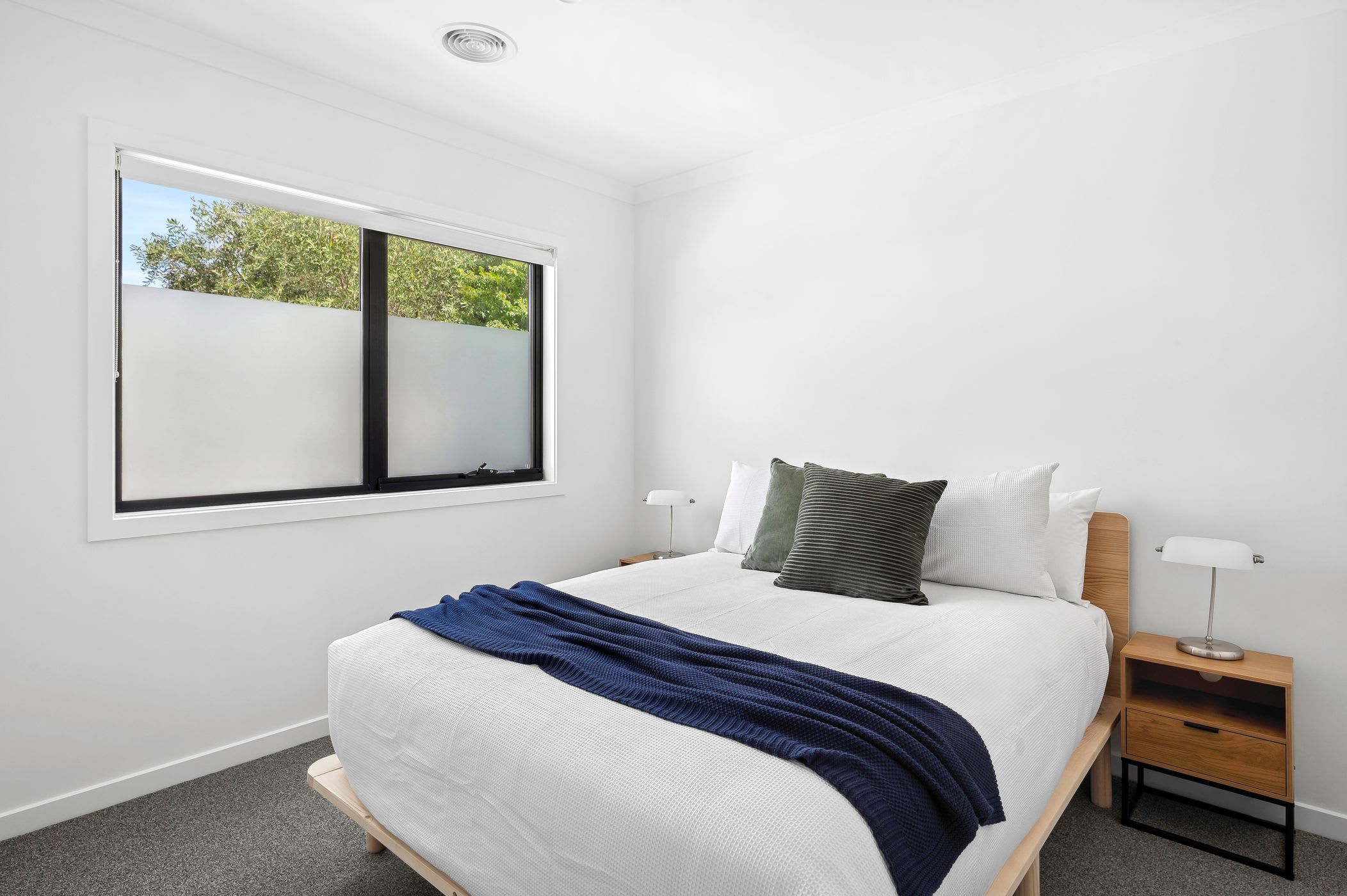 A bedroom with a large bed, a nightstand, a window, and a view of trees outside.