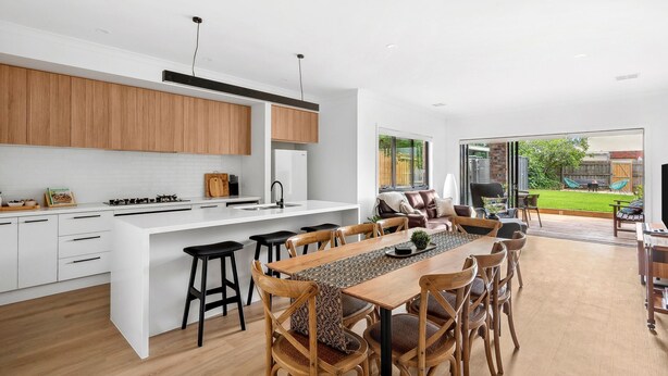 A modern kitchen with a large island, wooden cabinets, and a dining area with a long table and chairs. - St Helens I Stunning Family Townhouse in Geelong (Rippleside)