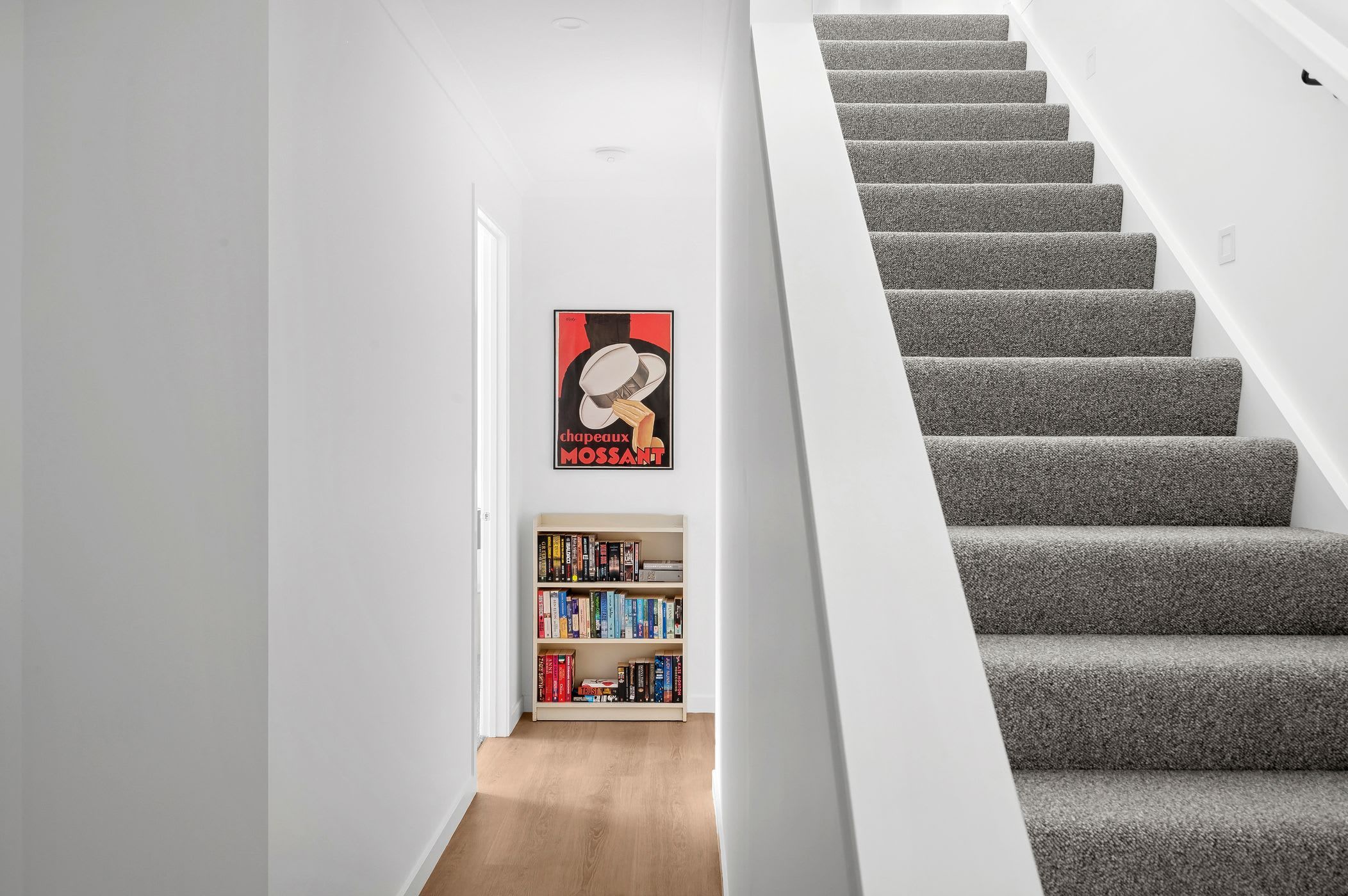 A staircase with grey carpeted steps leading to a landing. A bookshelf filled with books is visible on the landing.