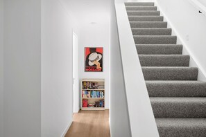 Una scala con gradini rivestiti di moquette grigia che porta a un pianerottolo. Si intravede una libreria piena di libri sul pianerottolo.