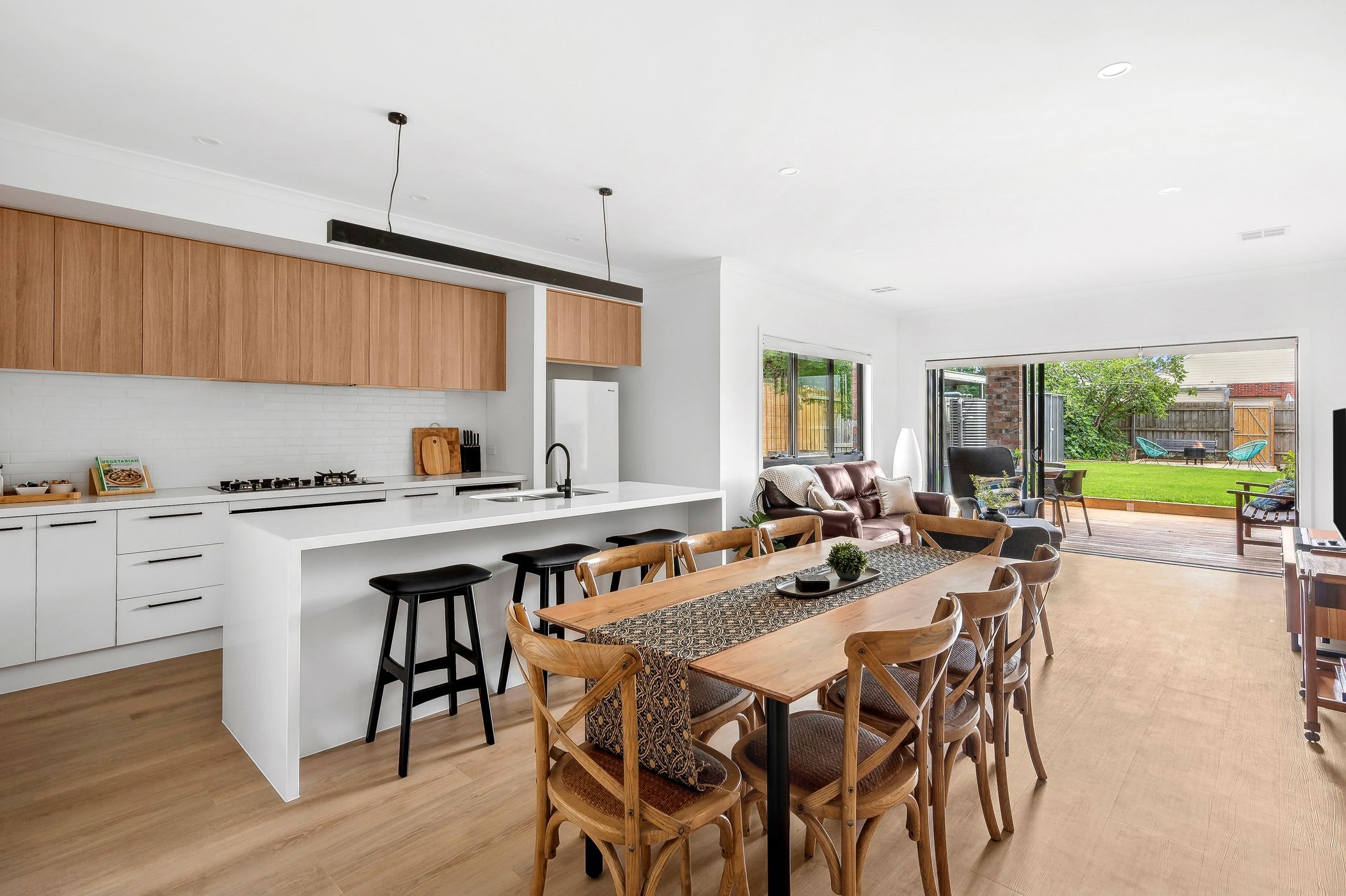 A modern kitchen with a large island, wooden cabinets, and a dining area with a long table and chairs.