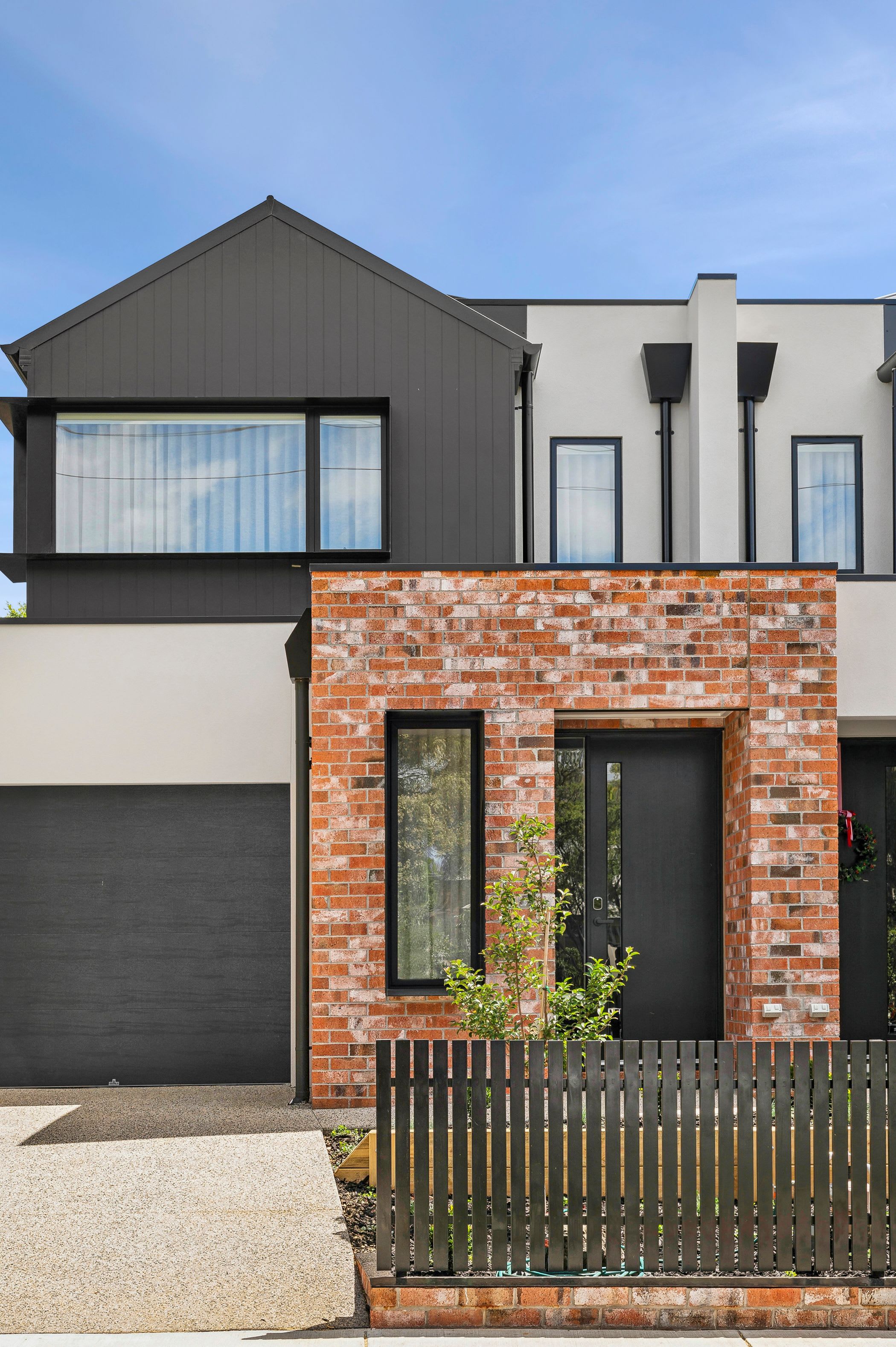 A modern two-story house with a brick facade and a dark grey roof.