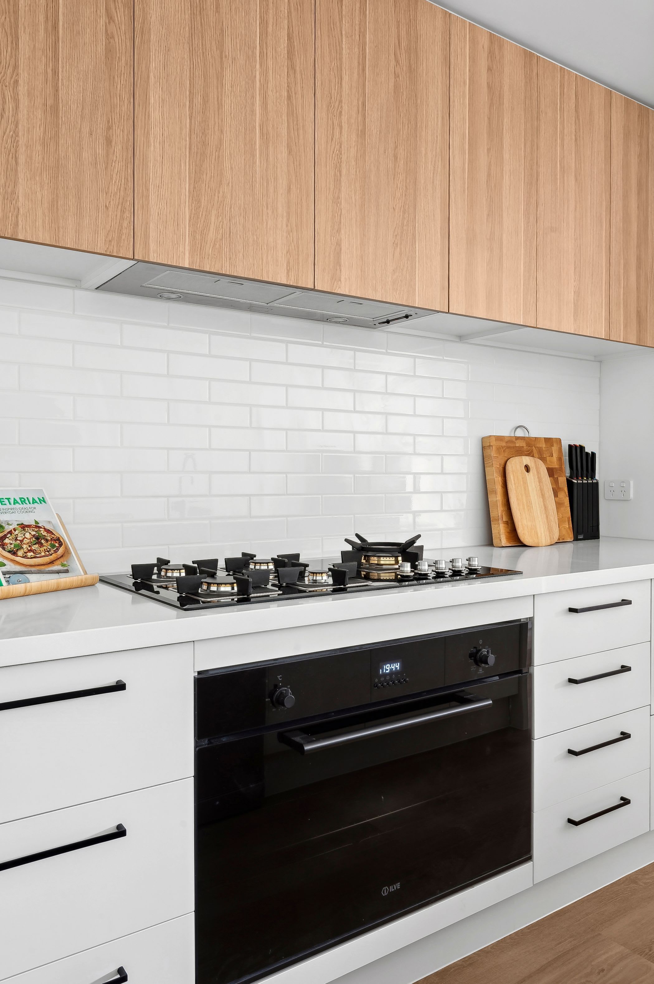 A modern kitchen with white cabinets, a black oven, and a gas stove.