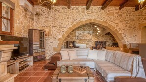 A rustic stone-walled living room with a large sofa, a wooden cabinet, and a fireplace.