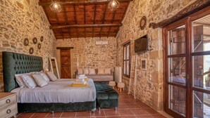 A bedroom with a stone wall, a wooden ceiling, a bed with a green upholstered headboard, and a large window.