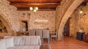 A rustic stone interior with a dining area, wooden ceiling, and a cozy seating arrangement.