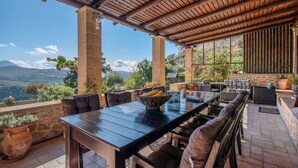 An outdoor patio with a wooden table and chairs, surrounded by stone walls and potted plants.