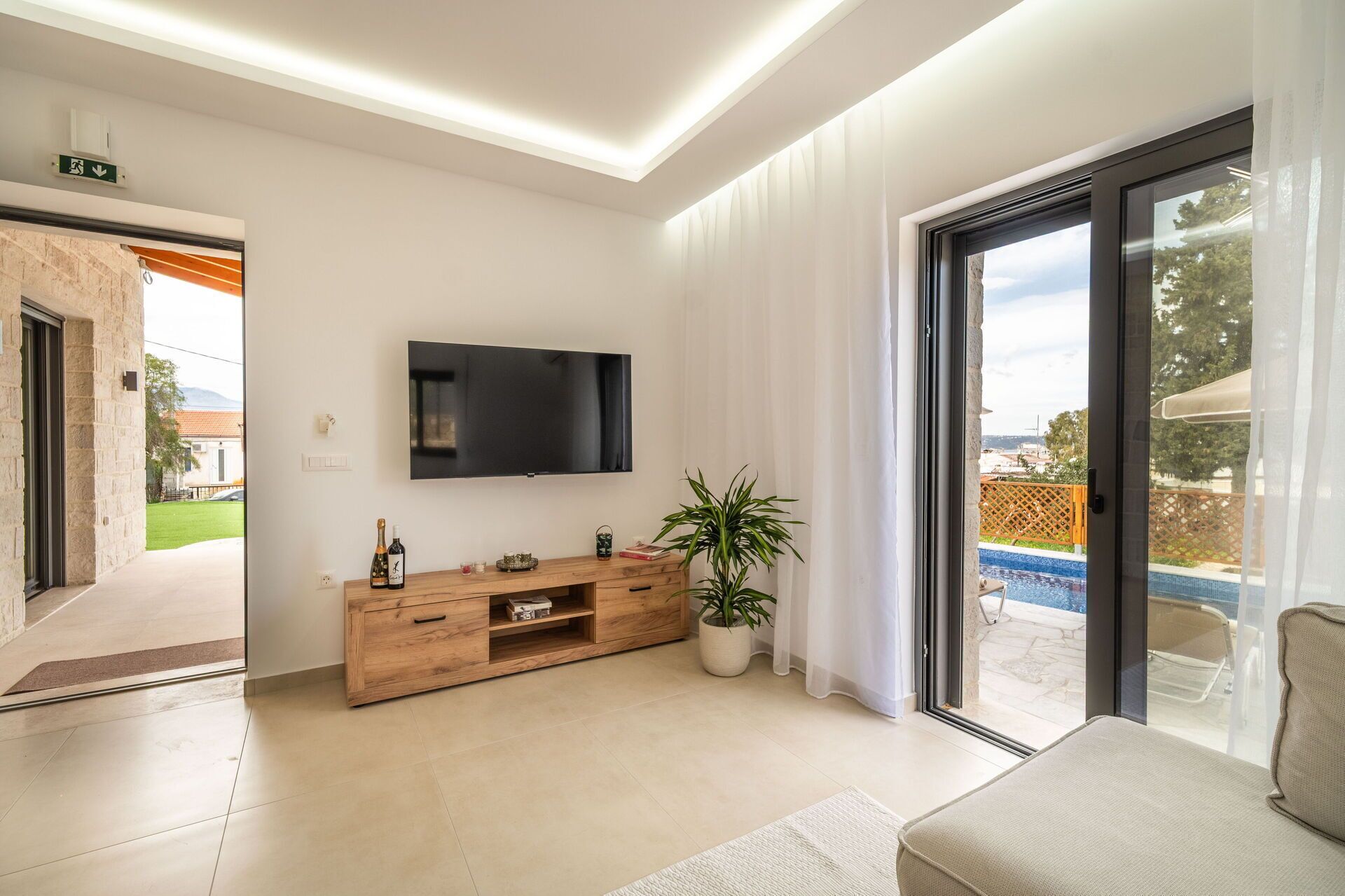 A modern living room with a flat-screen TV, wooden entertainment unit, and a potted plant.
