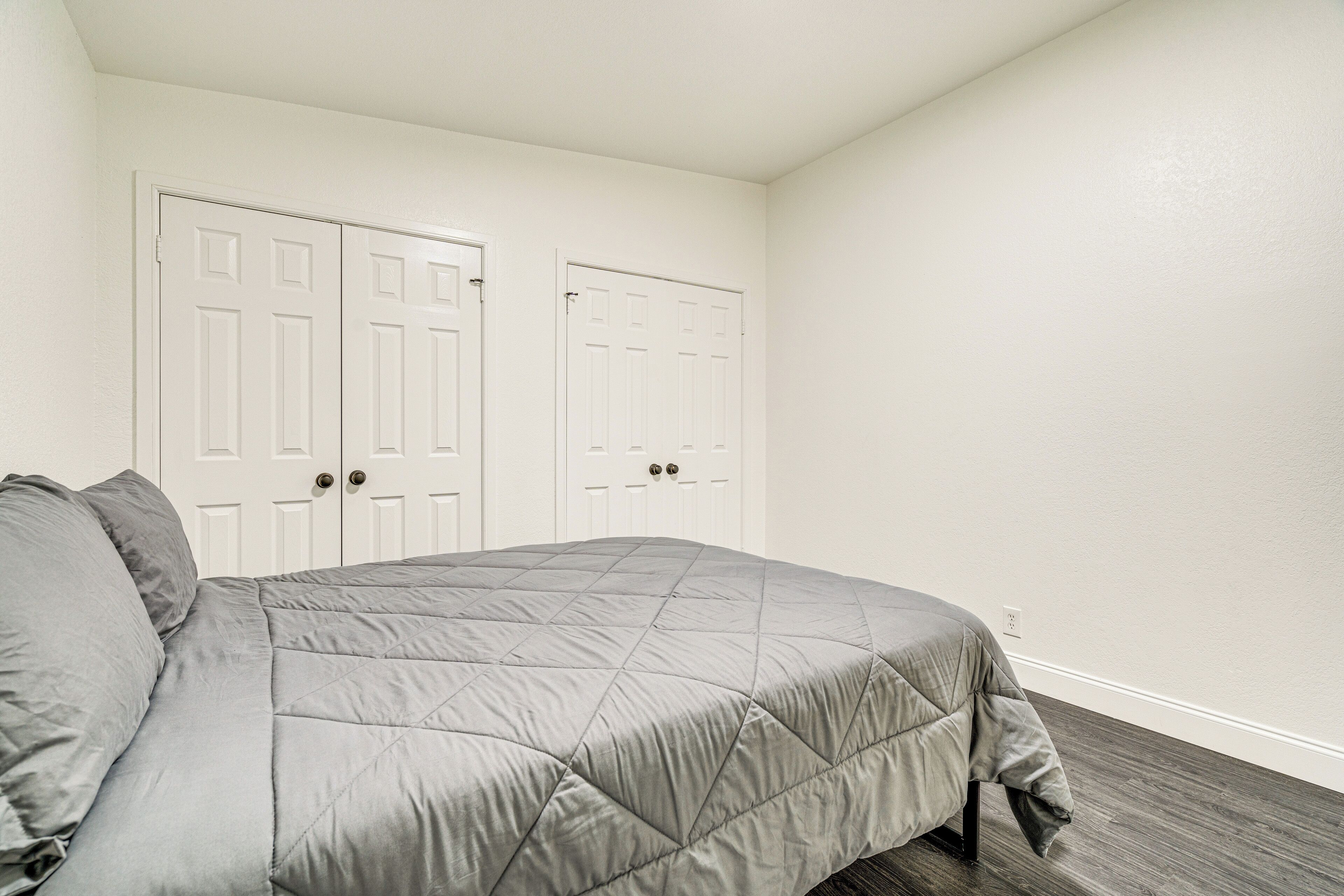 A bedroom with a bed, two white doors, and a wooden floor.